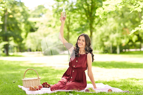 Image of happy woman with picnic basket and drink at park