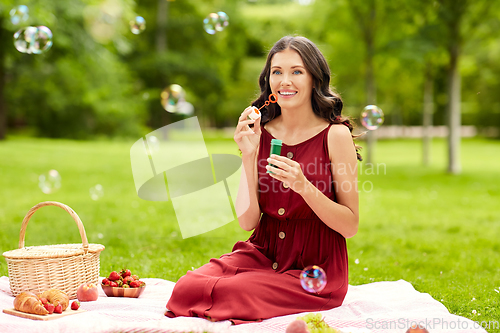 Image of happy woman blowing soap bubbles at picnic