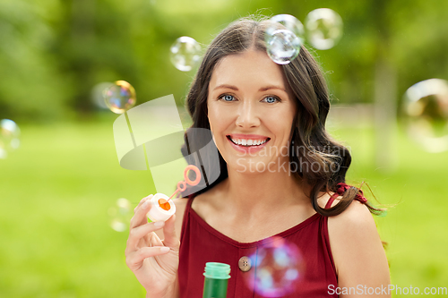 Image of happy woman blowing soap bubbles at summer park