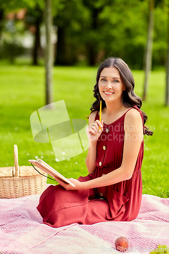 Image of happy woman with diary and picnic basket at park