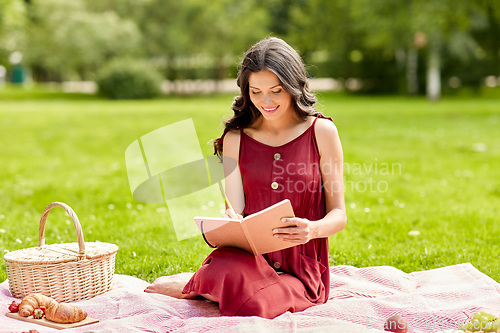 Image of happy woman with diary and picnic basket at park