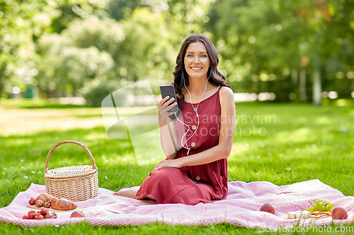 Image of woman with smartphone and earphones at picnic