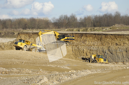 Image of Yellow dump trucks and excavator are working in gravel pit