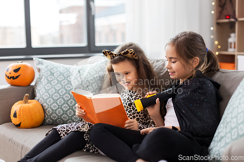 Image of girls in halloween costumes reading book at home