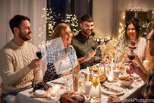 Image of happy friends drinking red wine at christmas party