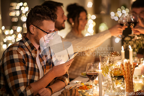 Image of man with smartphone at dinner party with friends