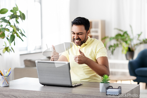 Image of happy indian man with laptop at home office