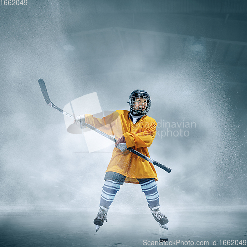 Image of Little hockey player with the stick on ice court in smoke. Sportsboy wearing equipment and helmet training in action.