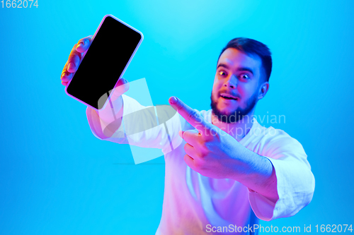 Image of Caucasian man\'s portrait isolated on blue studio background in neon light. Concept of human emotions, facial expression, sales, ad.