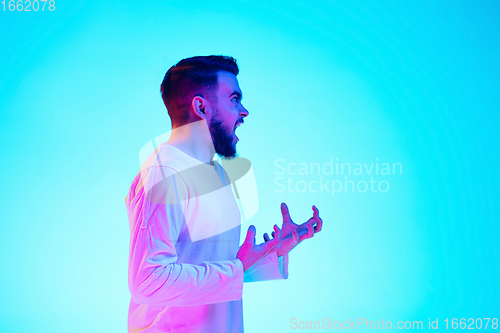 Image of Caucasian man\'s portrait isolated on blue studio background in neon light. Concept of human emotions, facial expression, sales, ad.