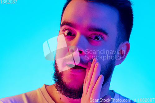 Image of Caucasian man\'s portrait isolated on blue studio background in neon light. Concept of human emotions, facial expression, sales, ad.