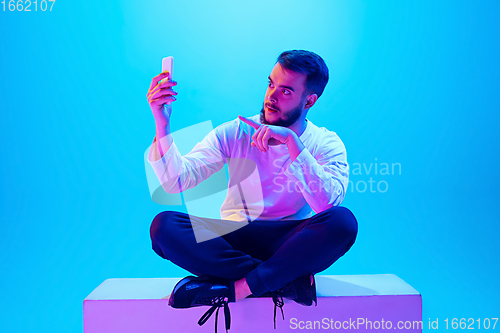 Image of Caucasian man\'s portrait isolated on blue studio background in neon light. Concept of human emotions, facial expression, sales, ad.