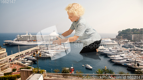 Image of See the world by children\'s eyes - little cute curly boy playing with big liner ship sitting on the city