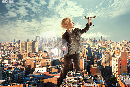 Image of See the world by children\'s eyes - little cute curly boy playing with airplane standing in the city