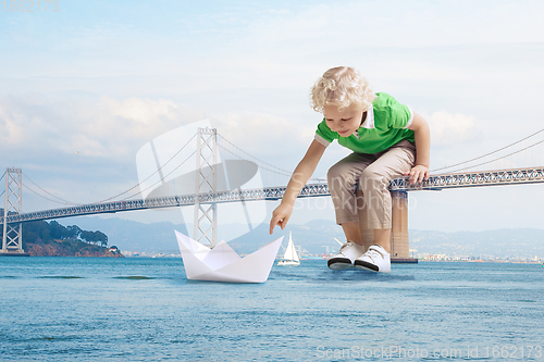 Image of See the world by children\'s eyes - little cute curly boy playing with paper ship sitting on bridge