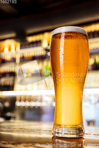 Image of Glass of lager beer on wooden table in warm light of bar