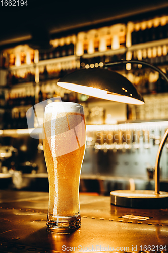 Image of Glass of lager beer on wooden table in warm light of bar
