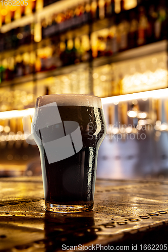 Image of Glass of stout beer on wooden table in warm light of bar