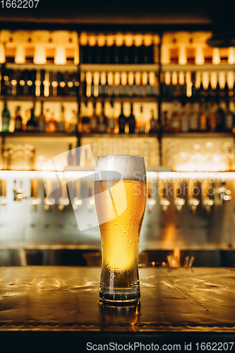 Image of Glass of lager beer on wooden table in warm light of bar