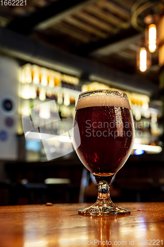 Image of Glass of stout beer on wooden table in warm light of bar