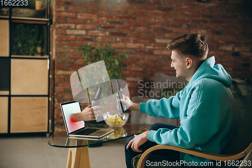 Image of Young man drinking beer during meeting friends on virtual video call. Distance online meeting, chat together on laptop at home.