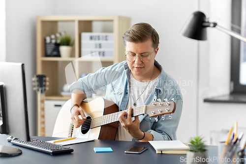 Image of young man playing guitar sitting at table at home