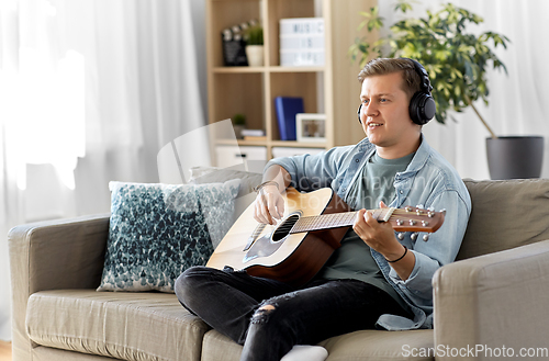 Image of man in headphones playing guitar at home
