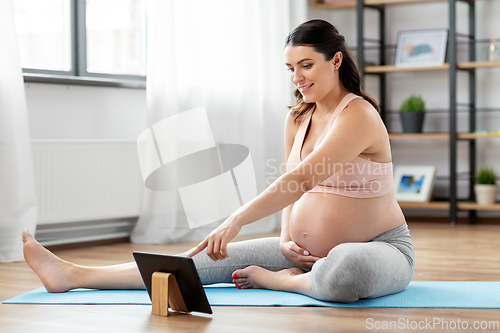 Image of pregnant woman with tablet pc doing sports at home
