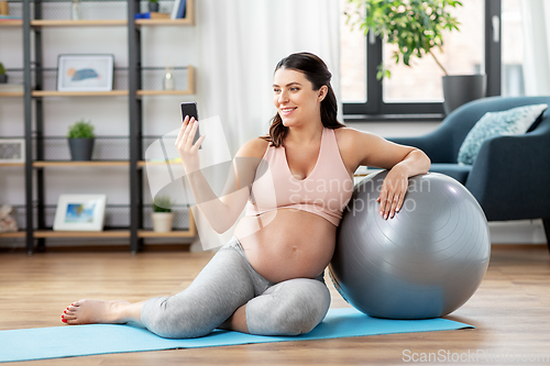 Image of pregnant woman with phone and fitness ball at home