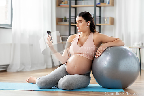 Image of pregnant woman with phone and fitness ball at home