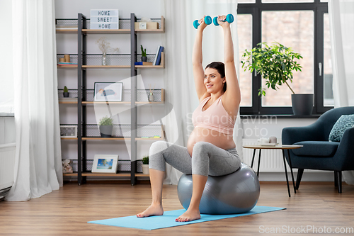 Image of pregnant woman with dumbbells doing sports at home