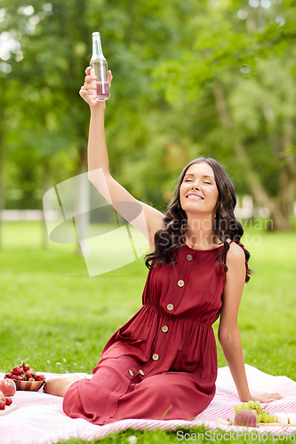 Image of happy woman toasting drink at picnic in park