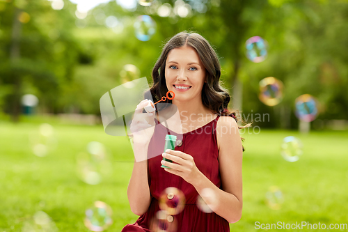 Image of happy woman blowing soap bubbles at summer park