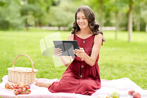 Image of happy woman with tablet computer on picnic at park