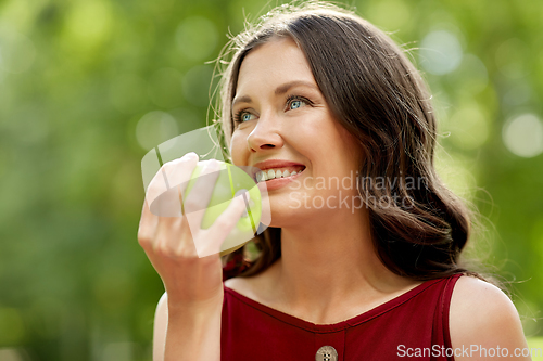 Image of happy woman eating green apple at summer park