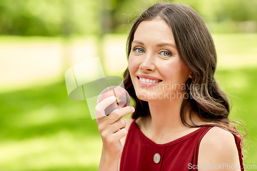 Image of happy woman eating peach at summer park