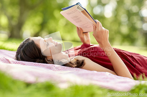 Image of happy woman reading book lying on blanket at park