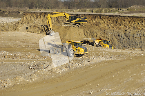 Image of Yellow dump trucks and excavator are working in gravel pit