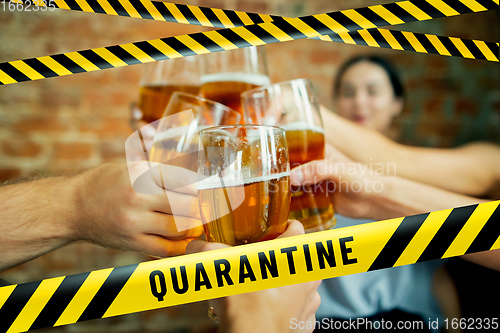 Image of Close up hands clinking glasses of beer at bar with bounding tapes Lockdown, Coronavirus, Quarantine, Warning - closing bars and nightclubs during pandemic