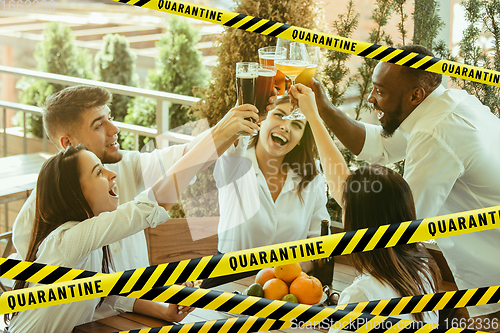 Image of Group of friends clinking glasses of beer at bar with bounding tapes Lockdown, Coronavirus, Quarantine, Warning - closing bars and nightclubs during pandemic