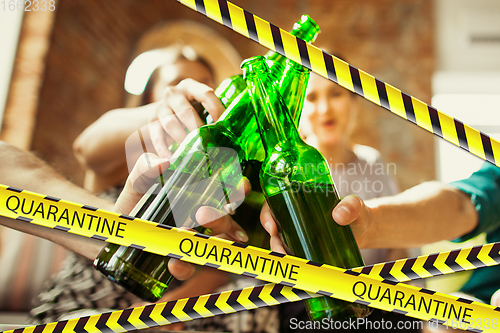 Image of Close up hands clinking bottles of beer at bar with bounding tapes Lockdown, Coronavirus, Quarantine, Warning - closing bars and nightclubs during pandemic