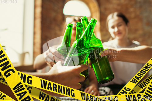 Image of Close up hands clinking bottles of beer at bar with bounding tapes Lockdown, Coronavirus, Quarantine, Warning - closing bars and nightclubs during pandemic