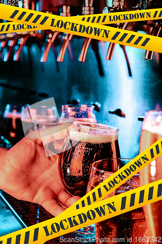 Image of Hand of bartender pouring a beer in tap with bounding tapes Lockdown, Coronavirus, Quarantine, Warning - closing bars and nightclubs during pandemic