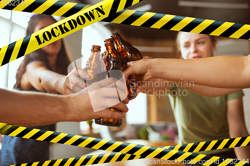 Image of Close up hands clinking bottles of beer at bar with bounding tapes Lockdown, Coronavirus, Quarantine, Warning - closing bars and nightclubs during pandemic