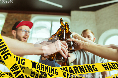 Image of Close up hands clinking bottles of beer at bar with bounding tapes Lockdown, Coronavirus, Quarantine, Warning - closing bars and nightclubs during pandemic