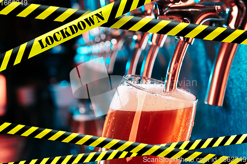 Image of Hand of bartender pouring a beer in tap with bounding tapes Lockdown, Coronavirus, Quarantine, Warning - closing bars and nightclubs during pandemic