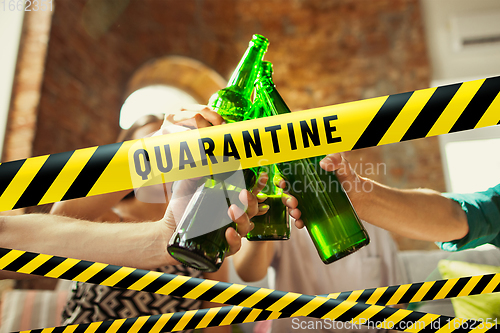 Image of Close up hands clinking bottles of beer at bar with bounding tapes Lockdown, Coronavirus, Quarantine, Warning - closing bars and nightclubs during pandemic