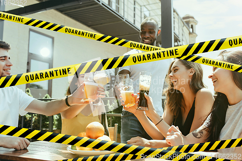 Image of Group of friends clinking glasses of beer at bar with bounding tapes Lockdown, Coronavirus, Quarantine, Warning - closing bars and nightclubs during pandemic