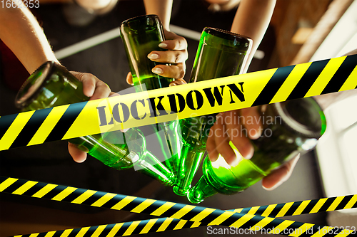 Image of Close up hands clinking bottles of beer at bar with bounding tapes Lockdown, Coronavirus, Quarantine, Warning - closing bars and nightclubs during pandemic