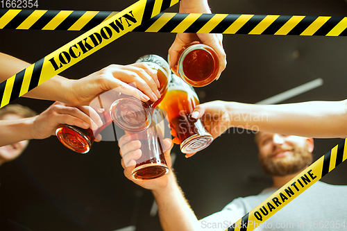 Image of Close up hands clinking glasses of beer at bar with bounding tapes Lockdown, Coronavirus, Quarantine, Warning - closing bars and nightclubs during pandemic
